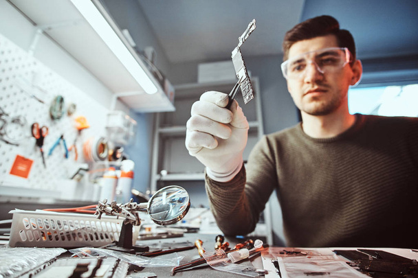 Мастер электронных технологий держит в ремонтной мастерской чип сломанного планшета
 - Фото, изображение
