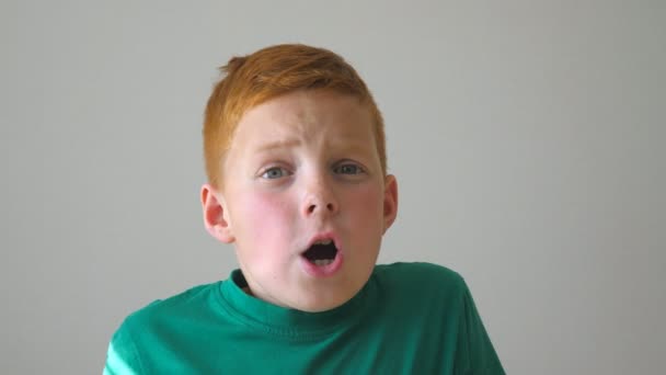 Close up of adorable red-haired boy grabbing his head and showing joy on his face. Hahdsome kid rejoicing achievement and giving a thumbs up. Portrait of happy boy with freckles indoor. Slow motion - Footage, Video