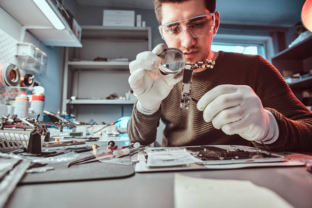 Electronic technician mending a broken tablet carefully examines the chip of the tablet using a magnifying glass - Фото, изображение