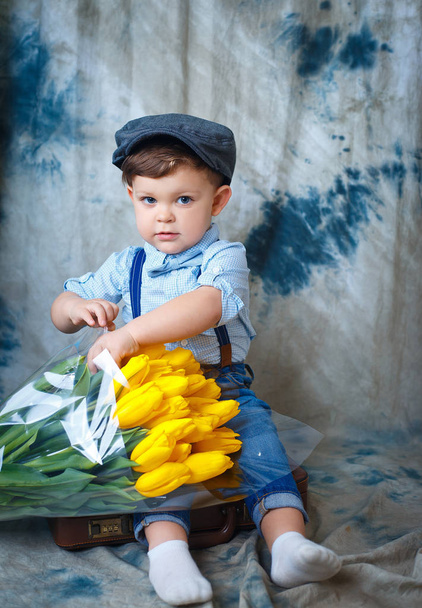 Funny curly baby with a bouquet of yellow tulips - Foto, Imagen