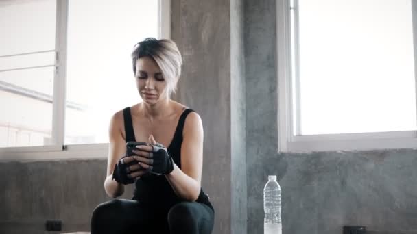 Authentic young caucasian woman using her mobile phone in gym to record and chatting to her friend, while resting. Fitness mobile technology concept. - Filmmaterial, Video