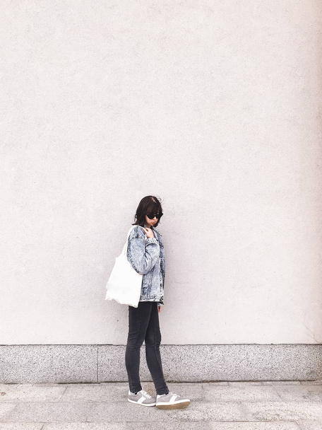 Стильна дівчина-хіпстер в джинсовому вбранні і сумці позує в місті
 - Фото, зображення