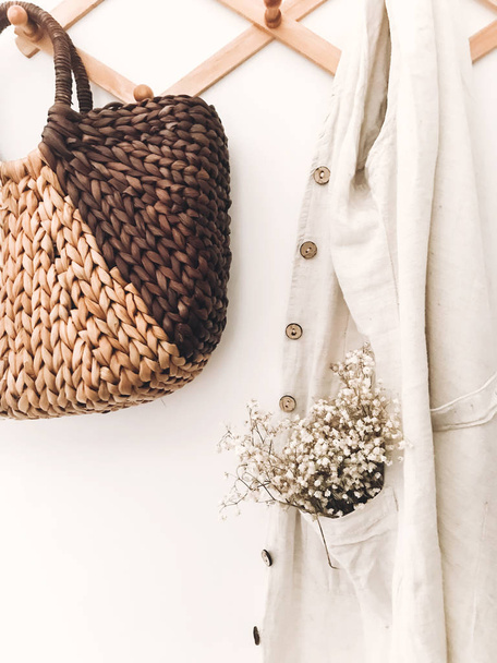 Stylish wooden hanger with straw bag, linen tote bag, flowers an - Foto, imagen