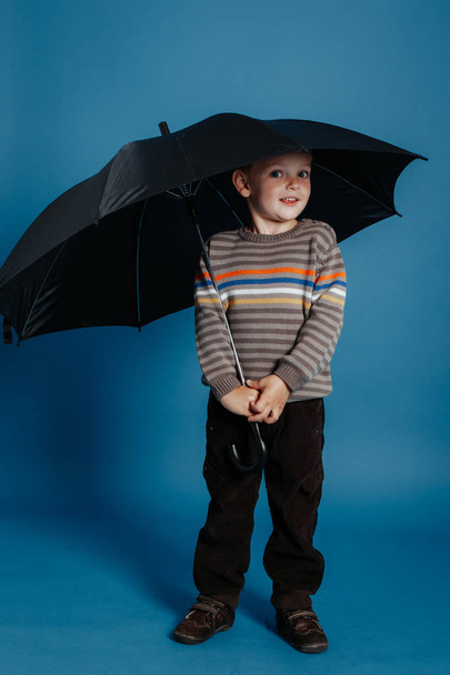 A little boy is standing under an open umbrella and smiling. - Photo, Image