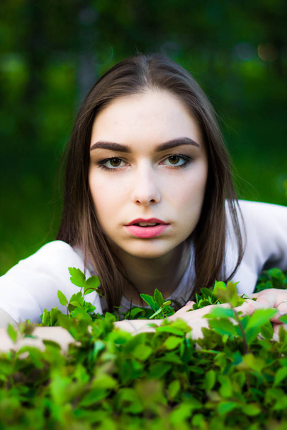 Portrait of a beautiful young woman on a background of green leaves, summer outdoors. Naturally beautiful woman smiling while standing among the green leaves. - Foto, afbeelding