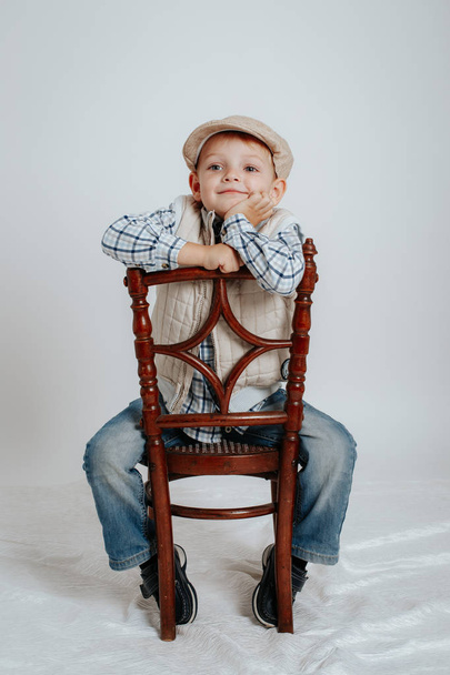 Little boy in a cap sits on a chair and smiles - Фото, изображение