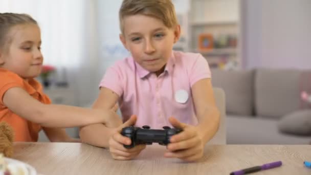 Little girl disturbing brother playing console game, children fighting joystick - Πλάνα, βίντεο