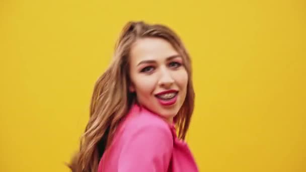 Young woman with long blond hair wearing a pink top dancing over a yellow studio background waving her arms to the music and moving towards the camera in a close up view. - Footage, Video