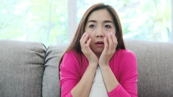 Young attractive asian woman sitting on couch at home watching a horror movie. Scarely mood. Lonely woman life style concept. - Materiaali, video