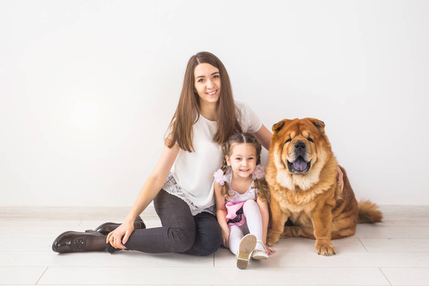 Kisállat, a gyermekek és a család fogalma - a kislány és anyja átölelve chow-chow kutyája felett fehér háttér - Fotó, kép