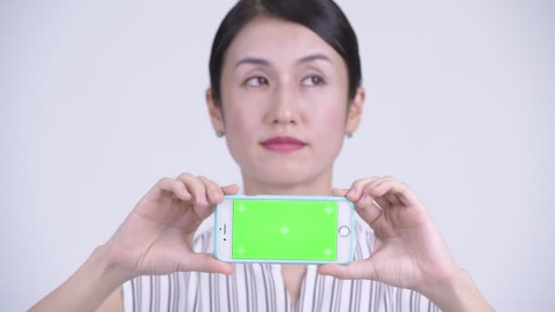 Face of happy beautiful Asian businesswoman thinking while showing phone - Video