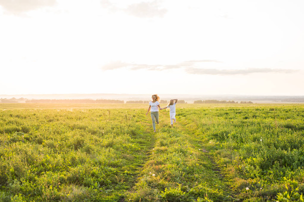 Family, summer and holiday concept - Mother holding her daughters hand running in green field - Фото, зображення