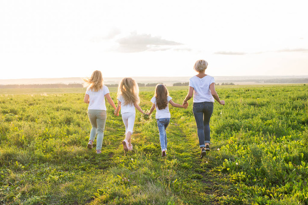 家族、夏休みなどの休暇のコンセプト - 女性と女の子が緑の野原で離れて行くのグループ - 写真・画像