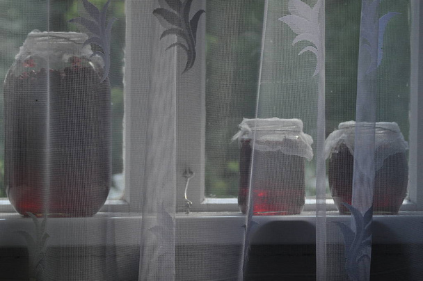Jar, słoiki dżemu z czerwonej porzeczki stoi na parapecie w gospodarstwie. Widok na ogród. - Zdjęcie, obraz