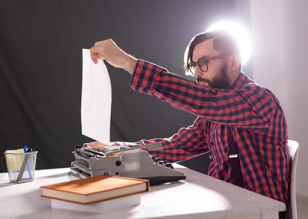 Menschen und Technologie-Konzept - Welttag des Schriftstellers, gutaussehender Mann mit Bart auf Schreibmaschine vor schwarzem Hintergrund - Foto, Bild