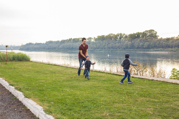 Childhood, family concept - father playing with two sons near the lake - Foto, afbeelding