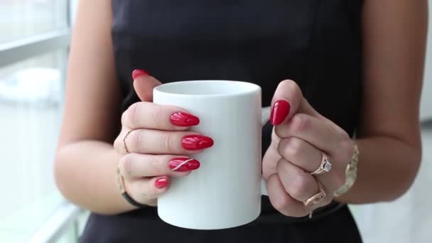 Vonzó fiatal nő az ablak mellett állandó, inni egy teát vagy kávét fehér kupa. - Felvétel, videó