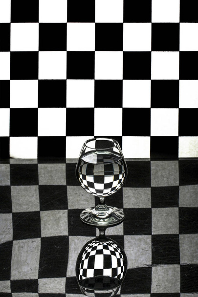 Abstract still life with a glass on a background of black and white cells - Photo, Image