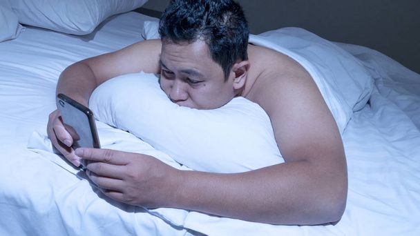 Τηλέφωνο εξαρτημένος έννοιας, Ασιατική άνθρωπο με έξυπνο τηλέφωνο στο κρεβάτι - Φωτογραφία, εικόνα