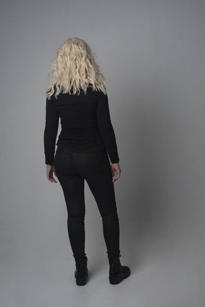 full length portrait of a blonde girl wearing  modern black jacket and pants, standing pose on grey studio background. - 写真・画像