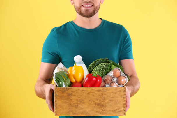 Delivery man holding wooden crate with food products on color background, closeup - Valokuva, kuva