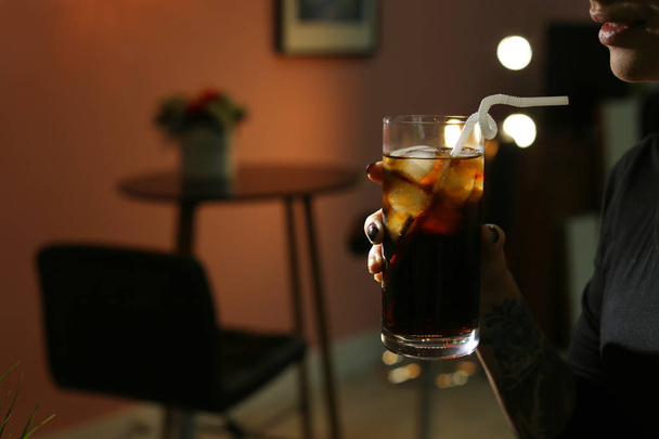 Woman with glass of cold cola in dark cafe, closeup. Space for text - Foto, Imagen