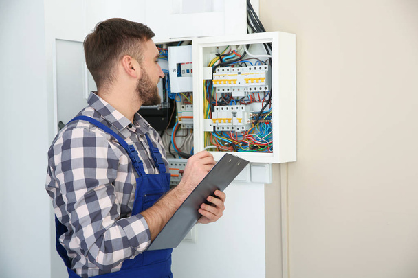 Male electrician with clipboard near fuse board indoors, space for text - Foto, immagini