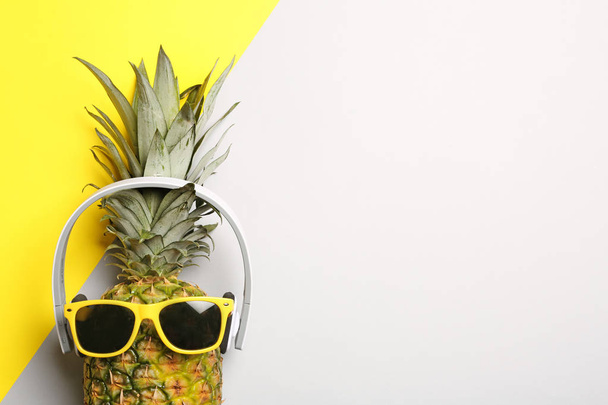 Funny pineapple with headphones and sunglasses on color background, top view. Space for text - Foto, Imagem