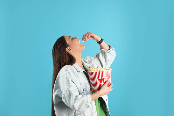 Young woman eating tasty popcorn on color background - Photo, Image