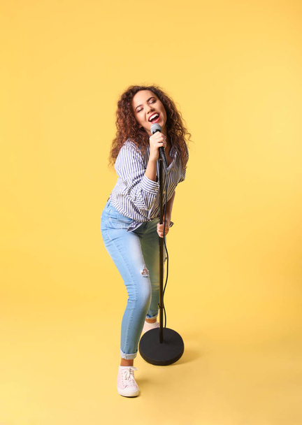 Curly African-American woman singing in microphone on color background - 写真・画像