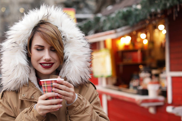 Woman with cup of mulled wine at winter fair. Space for text - 写真・画像