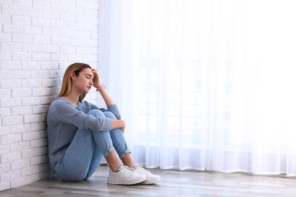 Emotional teenage girl sitting on floor indoors. Space for text - Foto, imagen