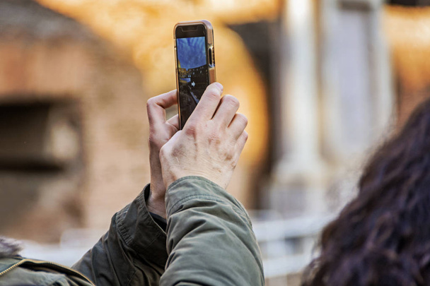 Hand holding smartphone taking picture in Colosseum stadium building in Rome - 写真・画像