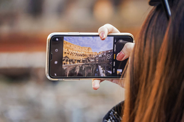 Hand holding smartphone taking picture in Colosseum stadium building in Rome - Foto, afbeelding