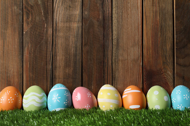 Colorful painted Easter eggs on green grass against wooden background, space for text - Fotografie, Obrázek