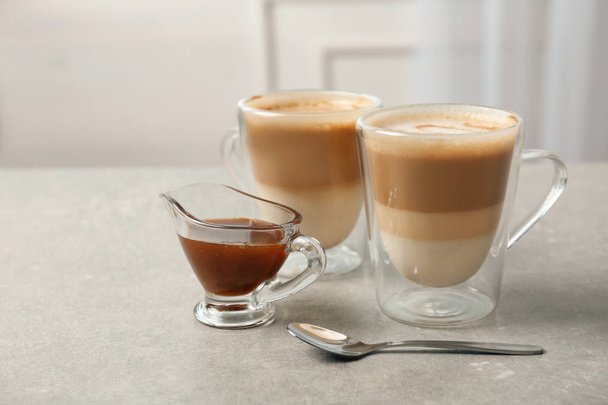 Glass cups of tasty caramel macchiato and gravy boat with syrup on table - Foto, Imagem