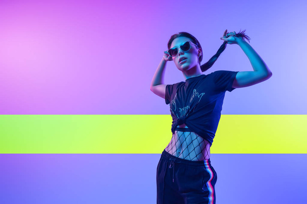 High-Fashion-Modell Frau in Mode T-Shirts und Hosen mit Streifen in den Farben lgbt in bunten hellen Neon UV-blauen und rosa Lichtern, posiert im Studio. Modekonzept und Zine-Kultur - Foto, Bild