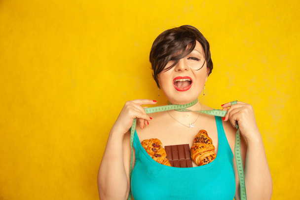 пухленькая девушка недовольная стандартами моды и грустная с сантиметровой лентой и высококалорийной едой, она плачет
 - Фото, изображение