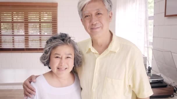 Asyalı yaşlı çift mutlu gülümseyerek duygu ve evde oturma odasında dinlenmek ise kameraya bakıyor. Evde kavramı zaman yaşam tarzı üst düzey aile zevk. Kameraya bakan portre. - Video, Çekim