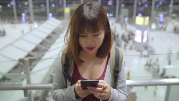 Heureuse Asiatique qui utilise et vérifie son smartphone dans le terminal en attendant son vol à la porte d'embarquement de l'aéroport international. Femmes heureux dans le concept de l'aéroport
. - Séquence, vidéo