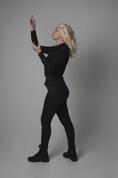 modern siyah ceket ve pantolon giyen bir sarışın kız ayakta poz gri studio arka plan üzerinde tam uzunlukta portresi. - Fotoğraf, Görsel