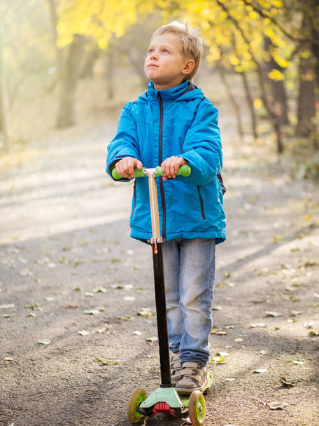 Ένα αγόρι Καβάλα ένα σκούτερ στο πάρκο φθινόπωρο. - Φωτογραφία, εικόνα