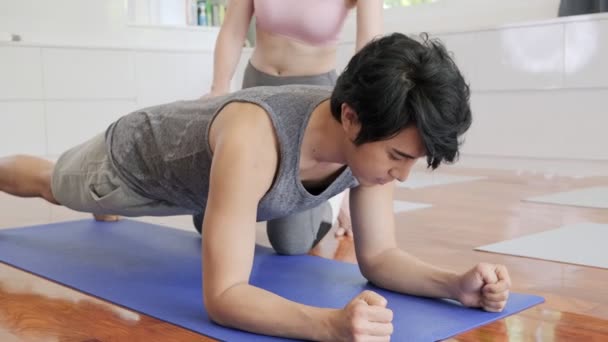 Beautiful asian woman personal trainer training young man yoga at home in living room. Healthly lifestyle concept. - Footage, Video