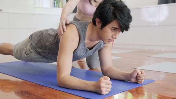 Beautiful asian woman personal trainer training young man yoga at home in living room, planking. Healthly lifestyle concept. - Filmagem, Vídeo