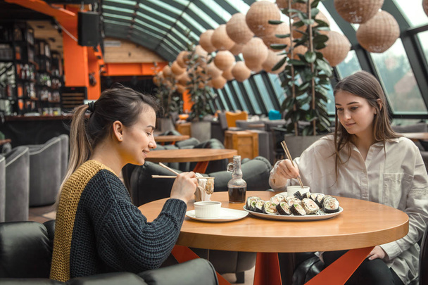 Twee gelukkige vrouwen zitten in een cafe, eten sushi - Foto, afbeelding