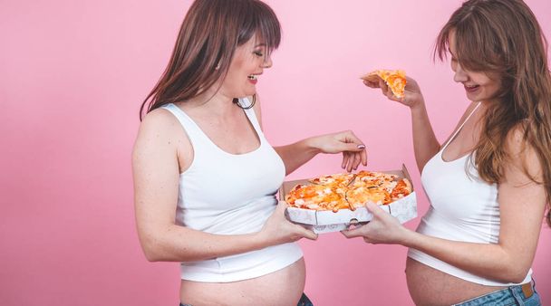 beslenme kavramı, hamile kadınlar pembe bir arka plan üzerinde pizza yemek - Fotoğraf, Görsel