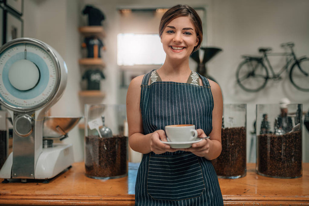 Young beautiful waitress smiling serving coffee with latte art  - Foto, afbeelding