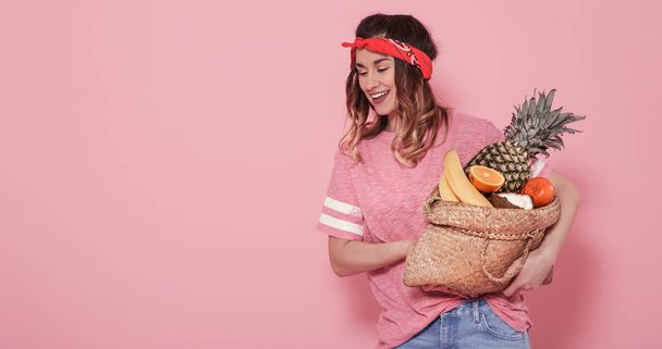 Портрет девушки с сумкой с фруктами, изолированными на розовой спине
 - Фото, изображение