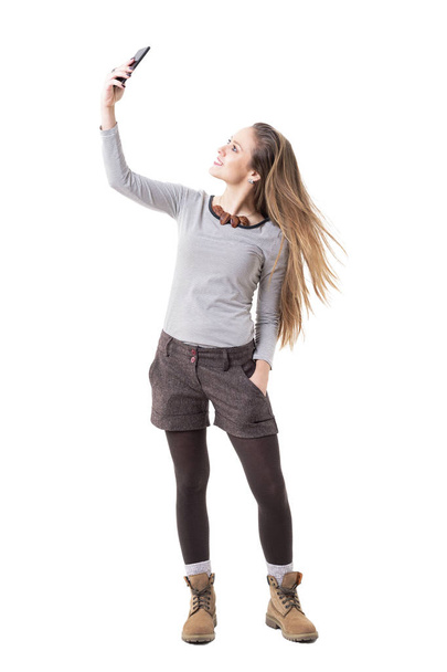 Happy nadšená dívka Mladé bokovky s selfie a odhodil dlouhé splývavé světlé vlasy. Celotělový izolovaných na bílém pozadí.  - Fotografie, Obrázek