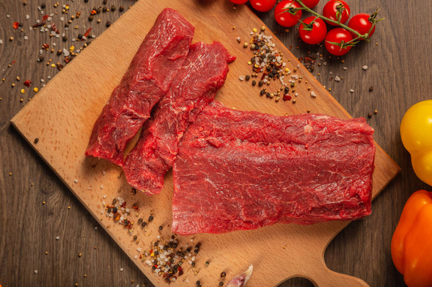 Syrové hovězí maso na dřevěné pozadí s kořením a zeleninou. - Fotografie, Obrázek
